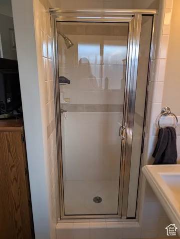 Shower enclosure featuring a chrome-framed glass door, white square wall tile with decorative mosaic inlay, and an integrated corner shelf