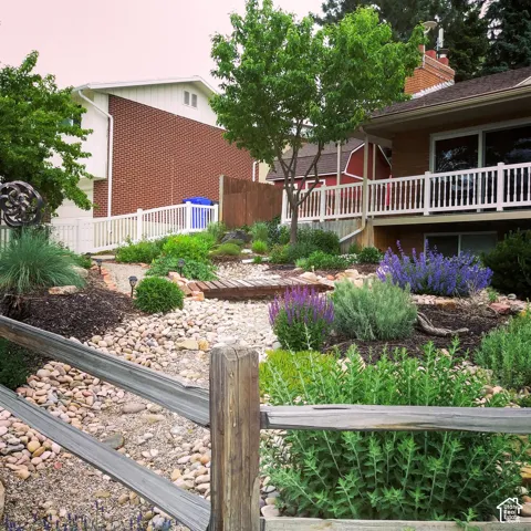 Landscaped backyard featuring a dry creek bed, decorative stone ground cover, a wooden footbridge, and a brick-accented exterior with an elevated deck