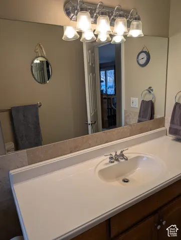 Vanity featuring a white molded countertop with an integrated sink, stone-finish backsplash, wood cabinetry, and a multi-bulb light fixture