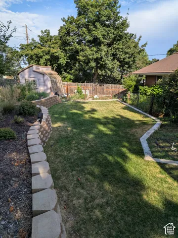 Backyard featuring a grass lawn, tiered stone retaining walls, mature trees, and a detached shed