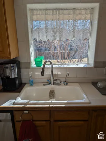 Double-basin drop-in sink with a high-arch gooseneck faucet, light-toned countertop, and white tile backsplash