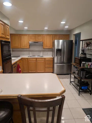 Kitchen featuring natural wood cabinetry, stainless steel refrigerator, built-in double oven, inset cooktop, and tile flooring