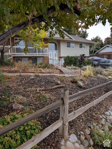 Split-level exterior featuring a brick and siding facade, elevated deck with a white railing, arched entryway, and wooden split-rail fencing
