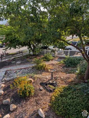 Landscaped front yard featuring mature trees, rock garden elements, perennial plantings, and a white picket fence