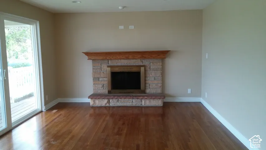 Fireplace featuring a stone surround, raised stone hearth, and natural wood mantel, complemented by wood-finish flooring and sliding glass doors
