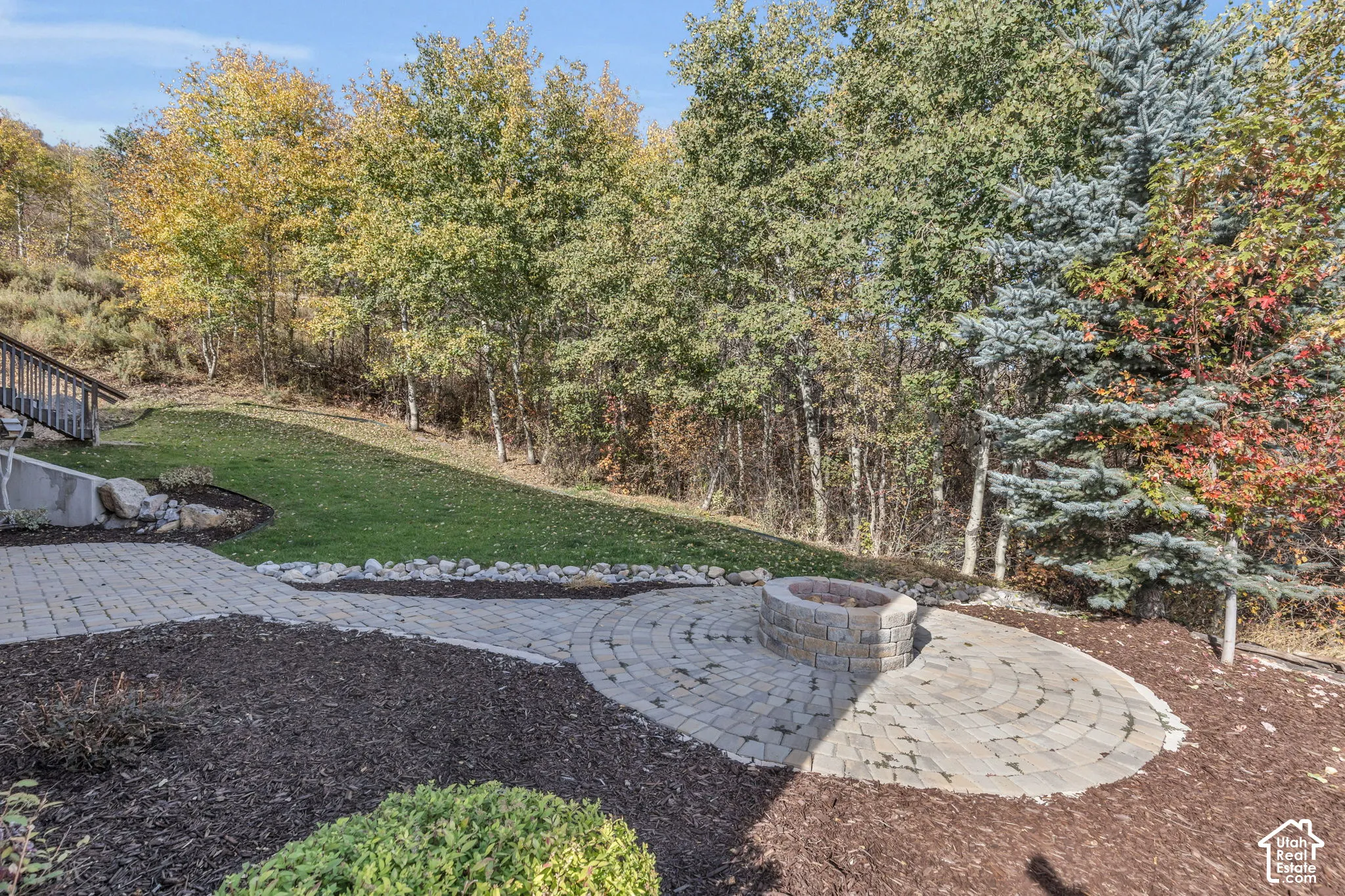Paver patio with a built-in fire pit, surrounded by mature trees and landscaped areas