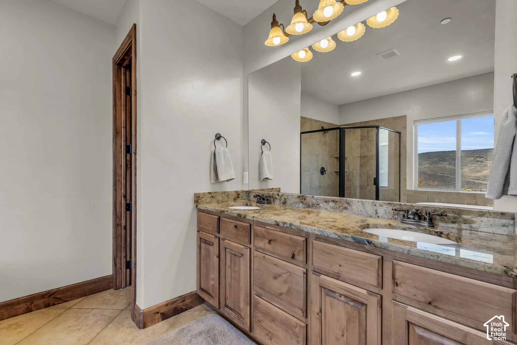 Dual sink vanity with a stone countertop, wood-finish cabinetry, and tiled flooring