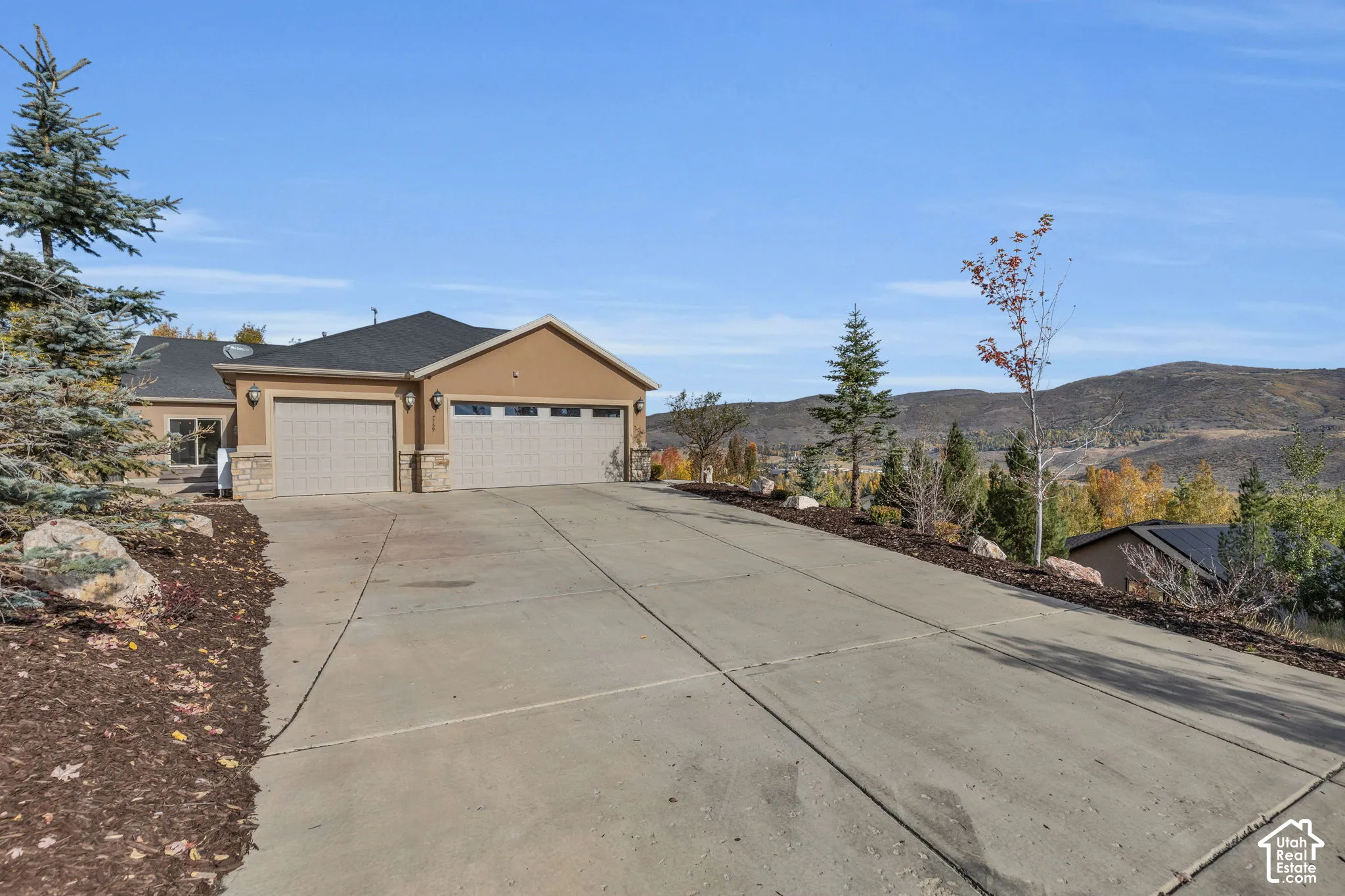 Two-car garage with stone accents, stucco exterior, and sloped concrete driveway