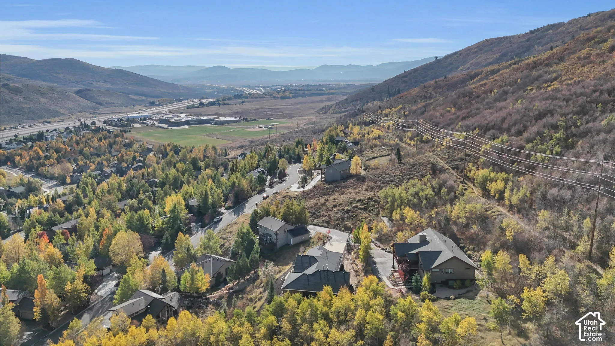 Hillside residential area with surrounding autumn foliage, mountainous backdrop, and distant highway infrastructure