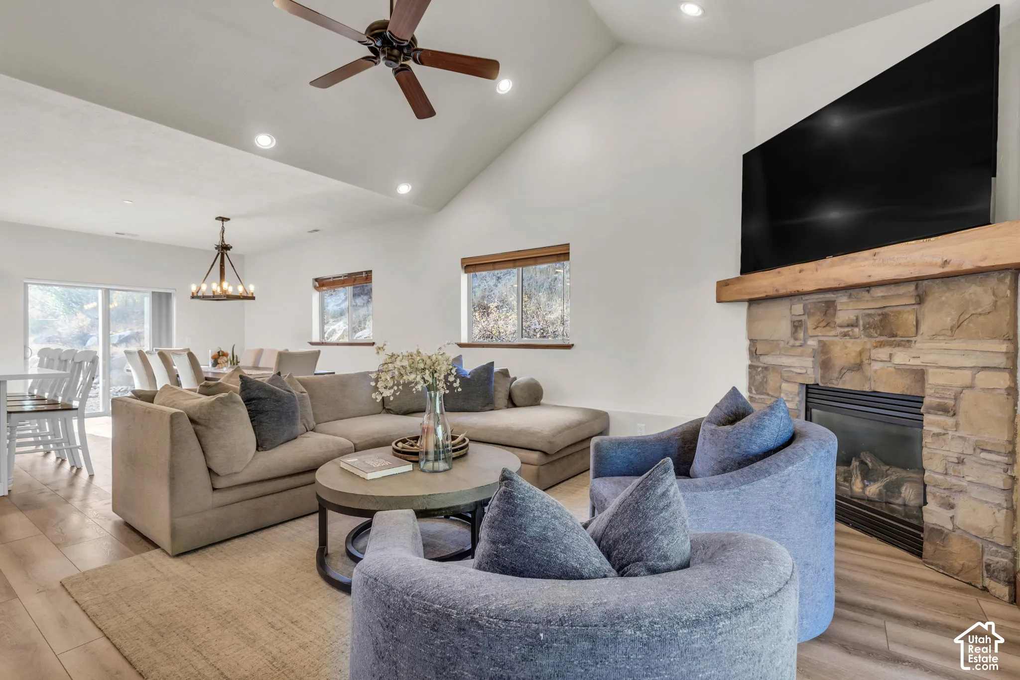 Vaulted ceiling with a ceiling fan, stone-faced fireplace with a wood mantle, recessed lighting, wood-finish flooring, and a sliding glass door