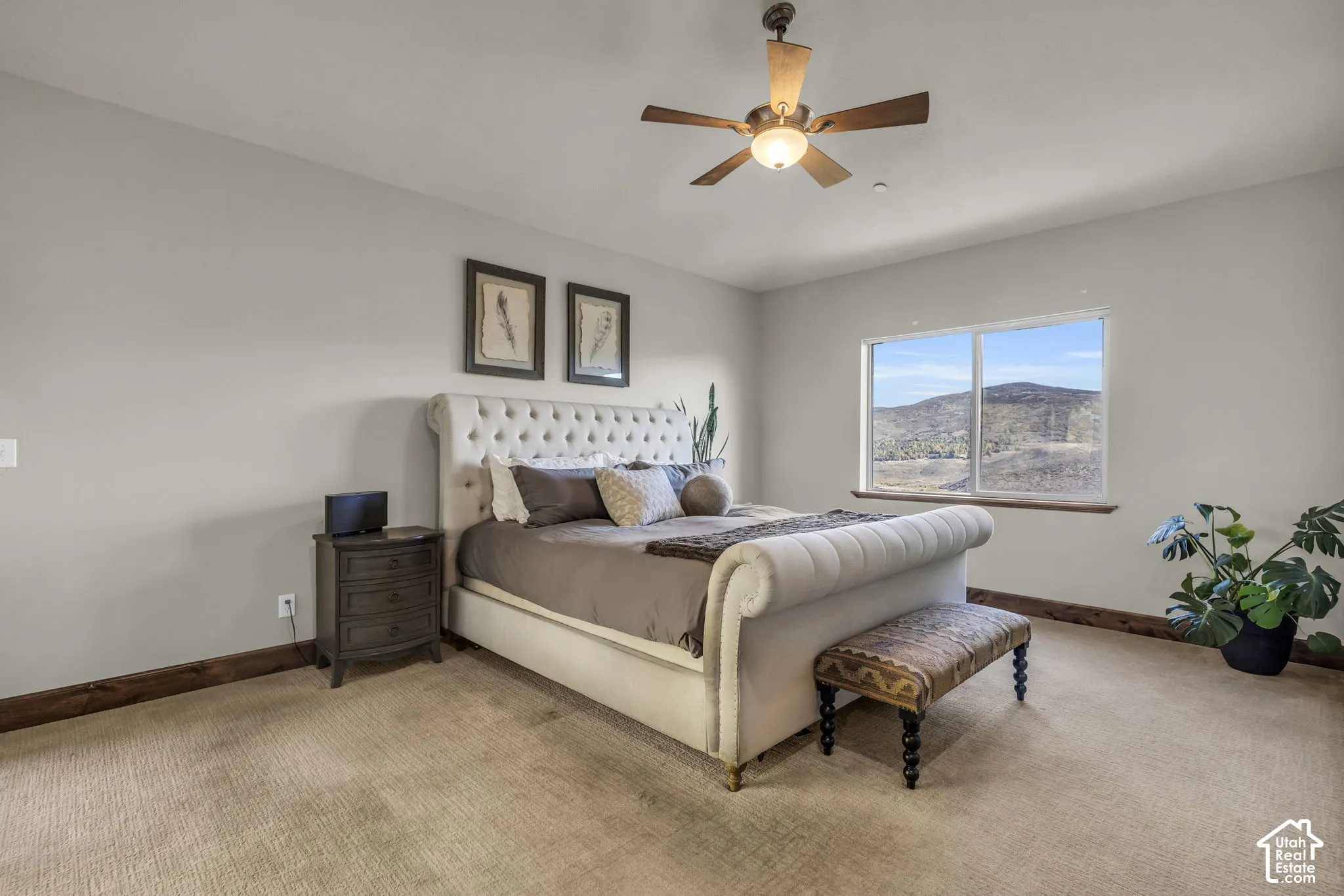 Bedroom with carpet flooring, neutral-toned walls, a ceiling fan with integrated lighting, and a large window featuring a mountain backdrop
