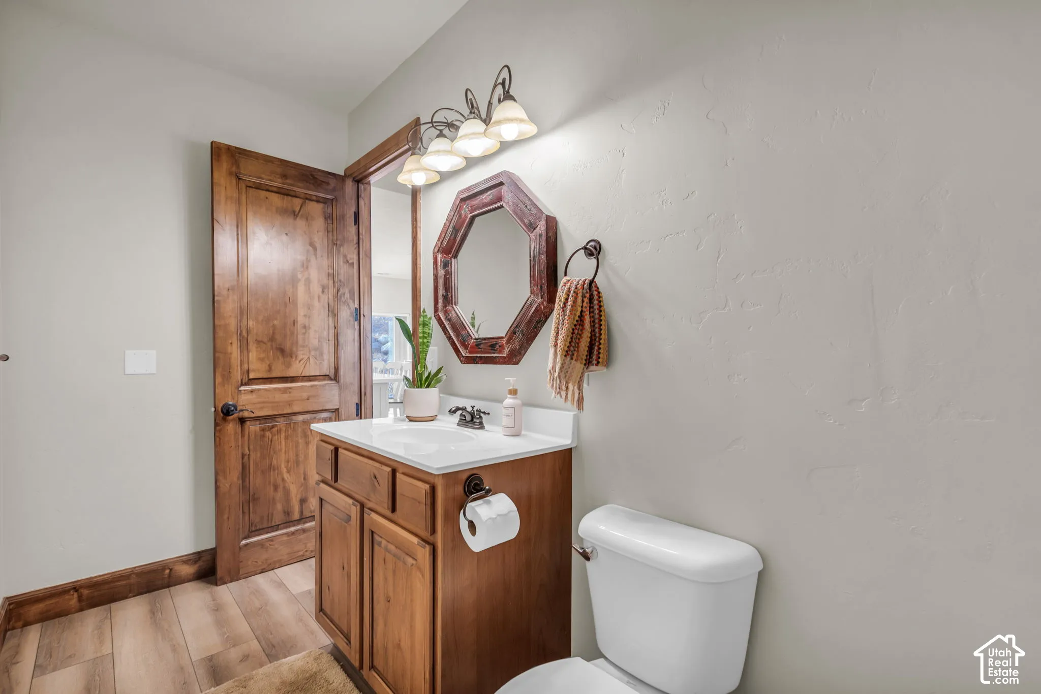Charming powder room showcasing warm wood cabinetry with an integrated sink vanity, decorative octagonal mirror, chrome dual-arm vanity lighting, and ceramic tile flooring