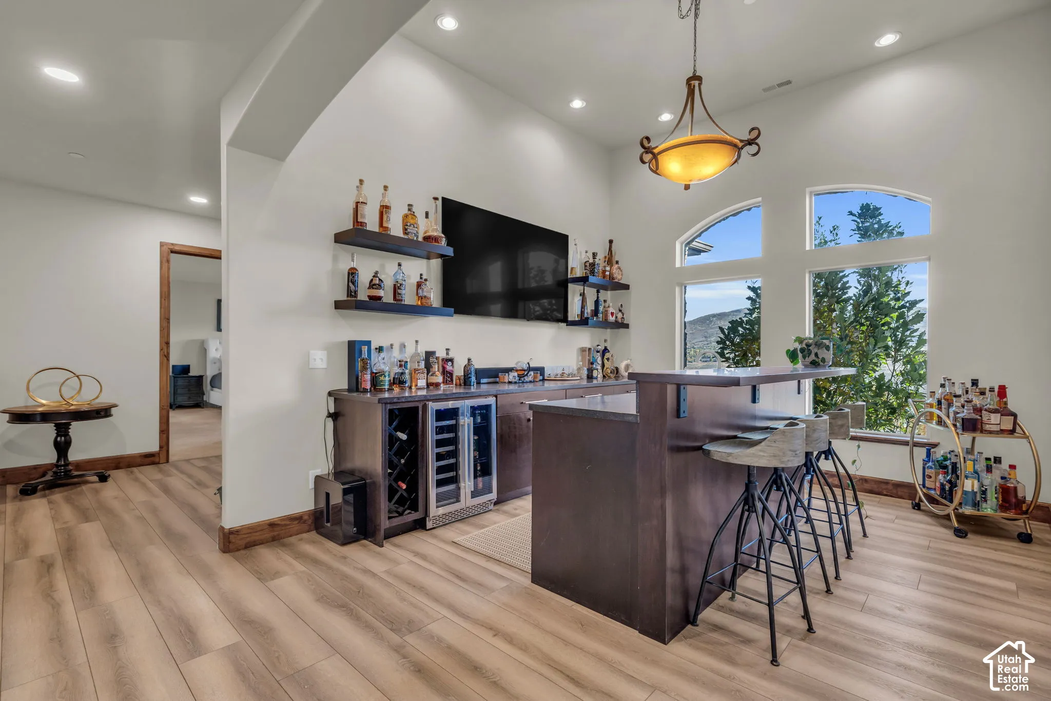 Wood-finish flooring, built-in bar with beverage refrigeration, pendant light fixture, and arched windows