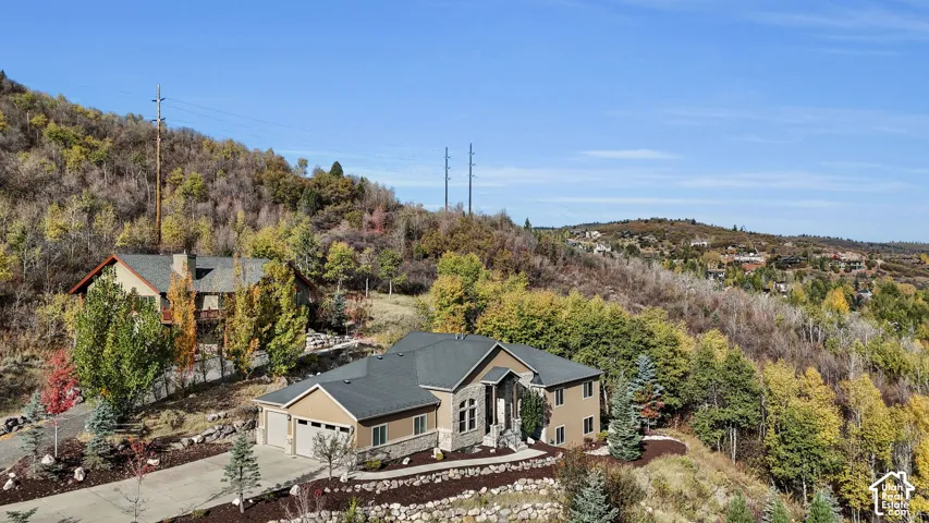 Expansive sloped property featuring a multi-level residence with an attached two-car garage, stone and stucco exterior, and a paved driveway