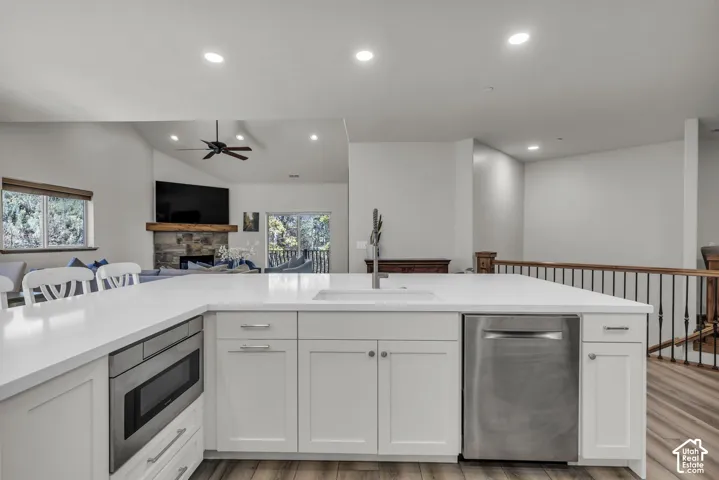 Kitchen island with white cabinetry, integrated stainless steel microwave, and undermount sink with a gooseneck faucet