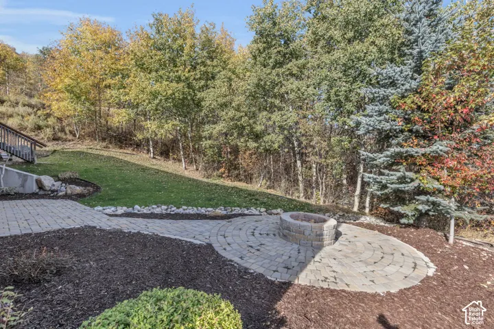 Paver patio with a built-in fire pit, surrounded by mature trees and landscaped areas