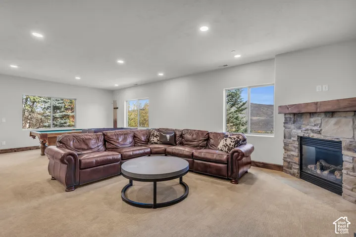 Spacious living room anchored by a curved leather sectional and round cocktail table, featuring recessed ceiling lighting, large windows framing mountain scenery, and a stone fireplace with built-in hearth