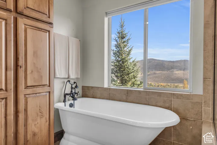 Freestanding soaking tub with a floor-mounted dark-finish faucet, custom wood-finish cabinetry, and a large window with mountain scenery