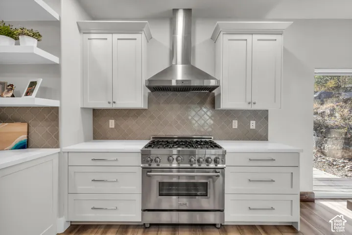 Chef's kitchen showcasing custom white cabinetry, professional-grade stainless steel range with six burners and convection oven, stainless steel range hood, quartz countertops, and geometric tile backsplash
