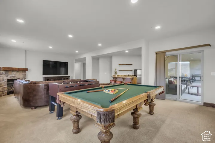 Recessed lighting throughout, stone fireplace with a wood mantle, built-in wet bar with shelving, glass sliding door, and neutral carpeting