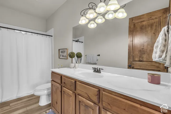 Wood-finish flooring, single vanity with a white countertop, wood-finish cabinetry, and a full mirror