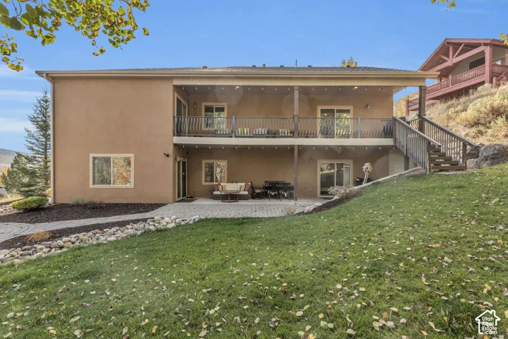 Exterior featuring a covered upper-level balcony with wood railings, a lower-level patio with paver stones, and a sloped grassy yard