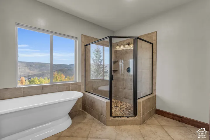 Freestanding bathtub, tiled shower enclosure with dark-framed glass, stone pebble shower floor, and a large window