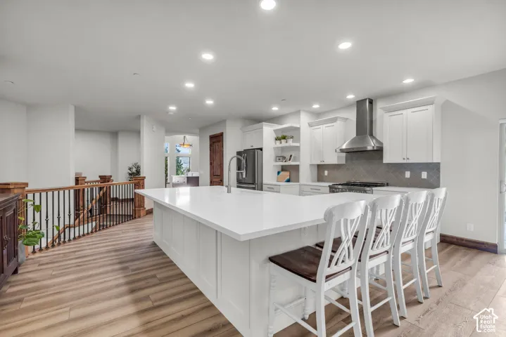 Open-concept kitchen with a large central island, white cabinetry, stainless steel range hood, and wood-finish flooring