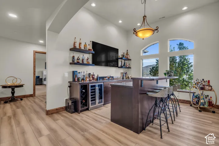 Wood-finish flooring, built-in bar with beverage refrigeration, pendant light fixture, and arched windows