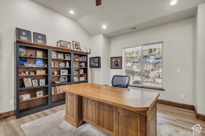 Vaulted ceiling with recessed lighting, built-in shelving, wood-finish flooring, and a large window