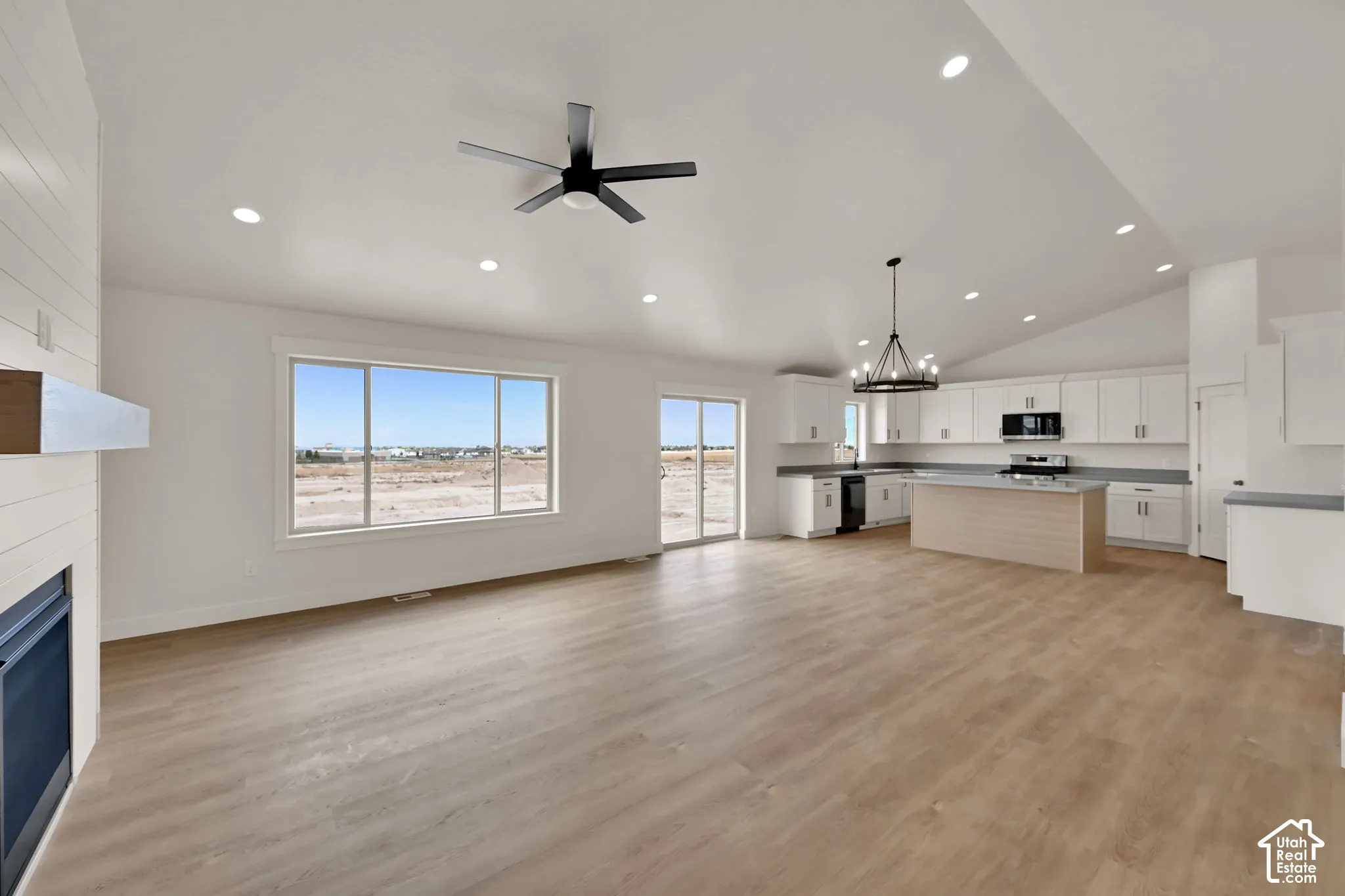 Open-concept interior featuring vaulted ceilings, wood-finish flooring, a kitchen island, recessed lighting, and a fireplace with shiplap detailing