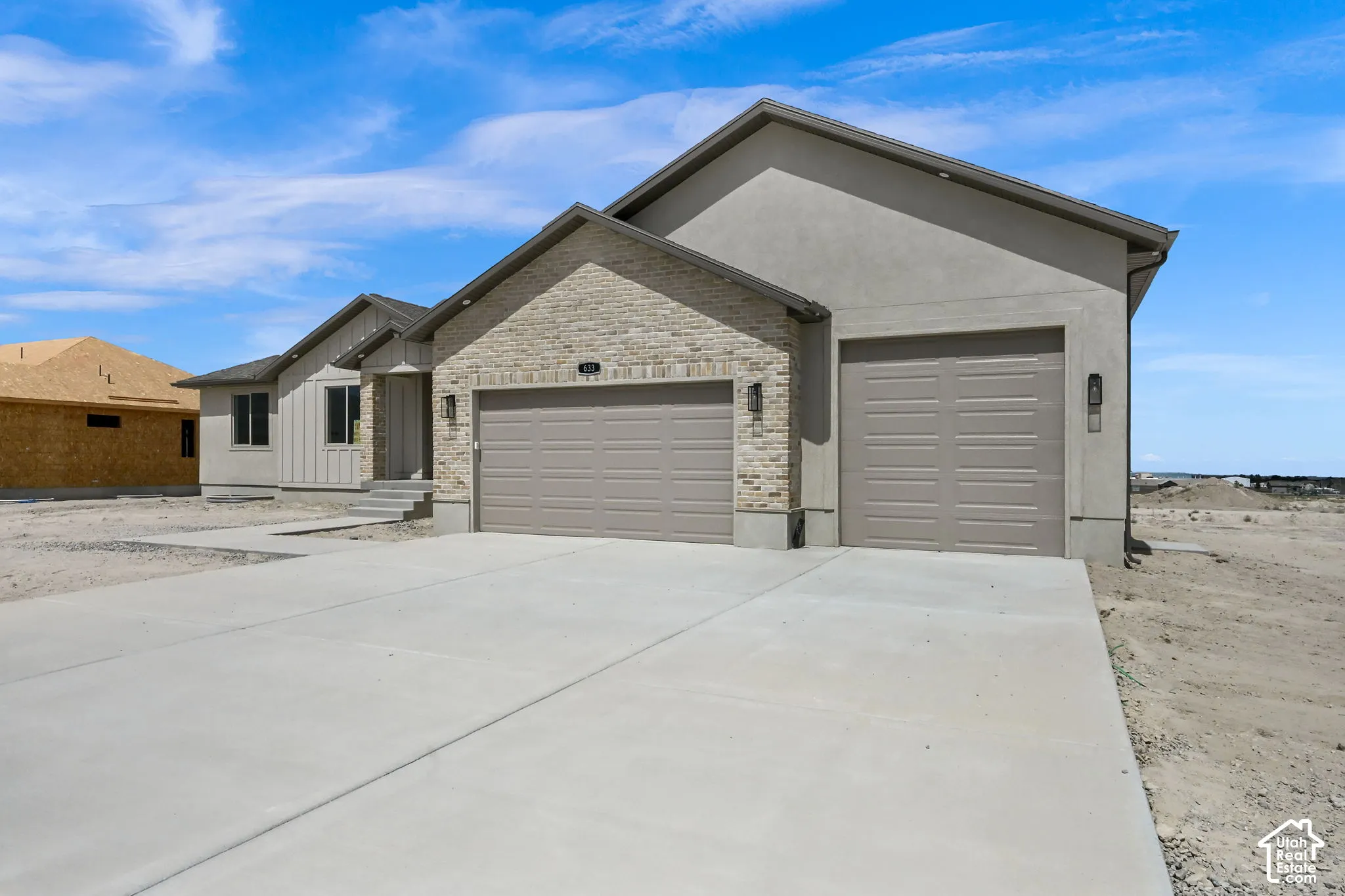Stucco exterior featuring stacked stone accents, dual garage doors, and a concrete driveway
