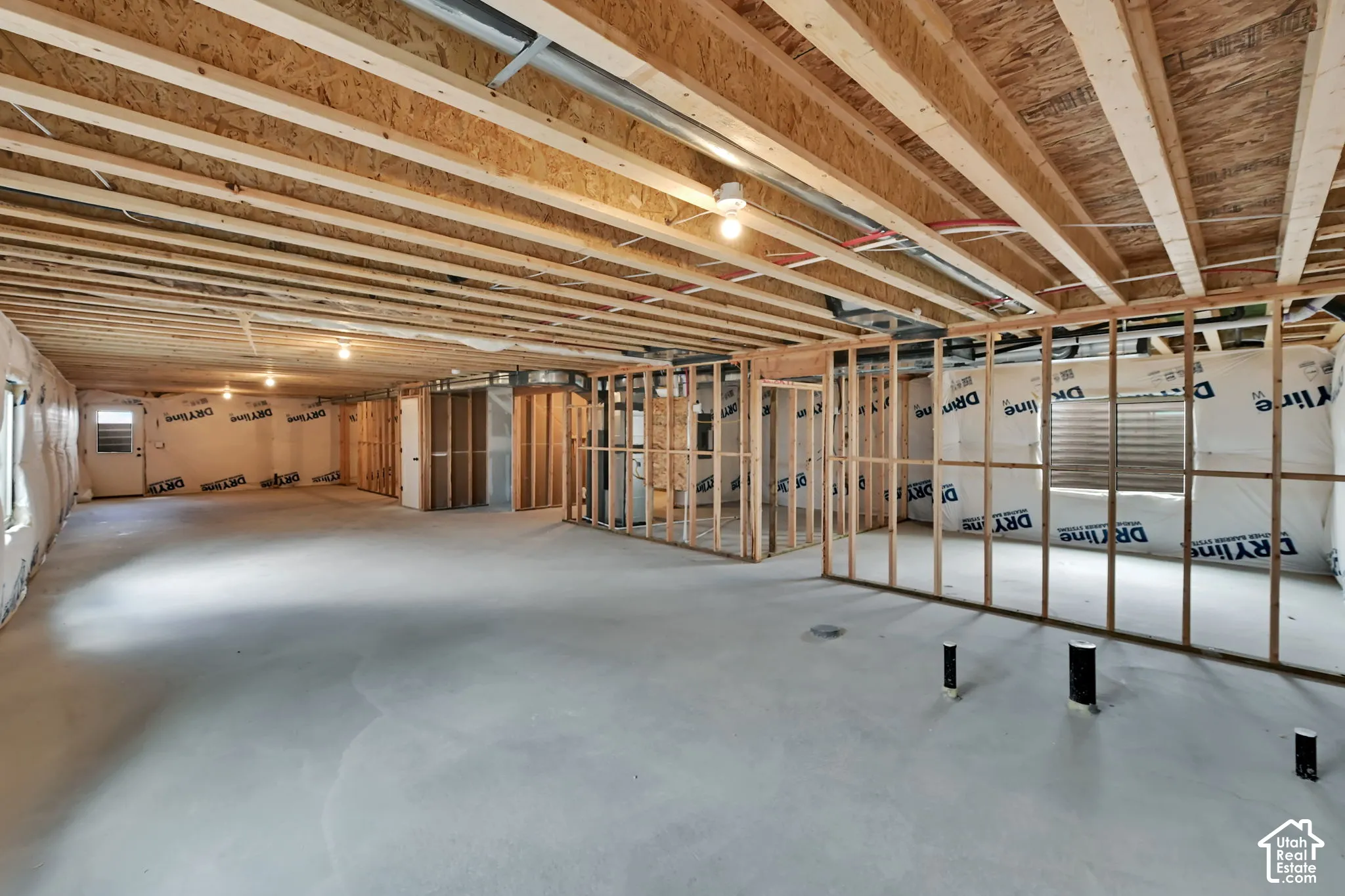Unfinished interior space featuring exposed wood joist ceilings, concrete flooring, stud-framed partition walls, and installed drainage plumbing