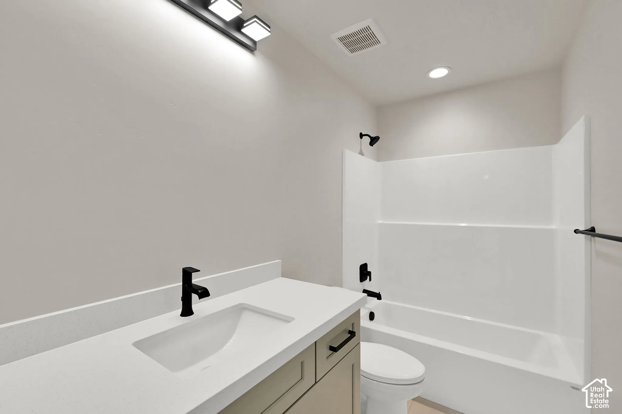 Bathroom featuring a vanity with a white countertop and rectangular undermount sink, matte black hardware, multi-bulb vanity light, and a white tub-shower surround