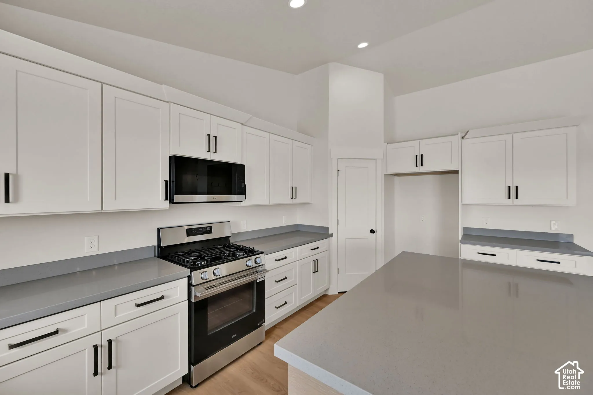 Kitchen featuring white shaker-style cabinetry, quartz countertops, a central island, stainless steel gas range, and wood-finish flooring