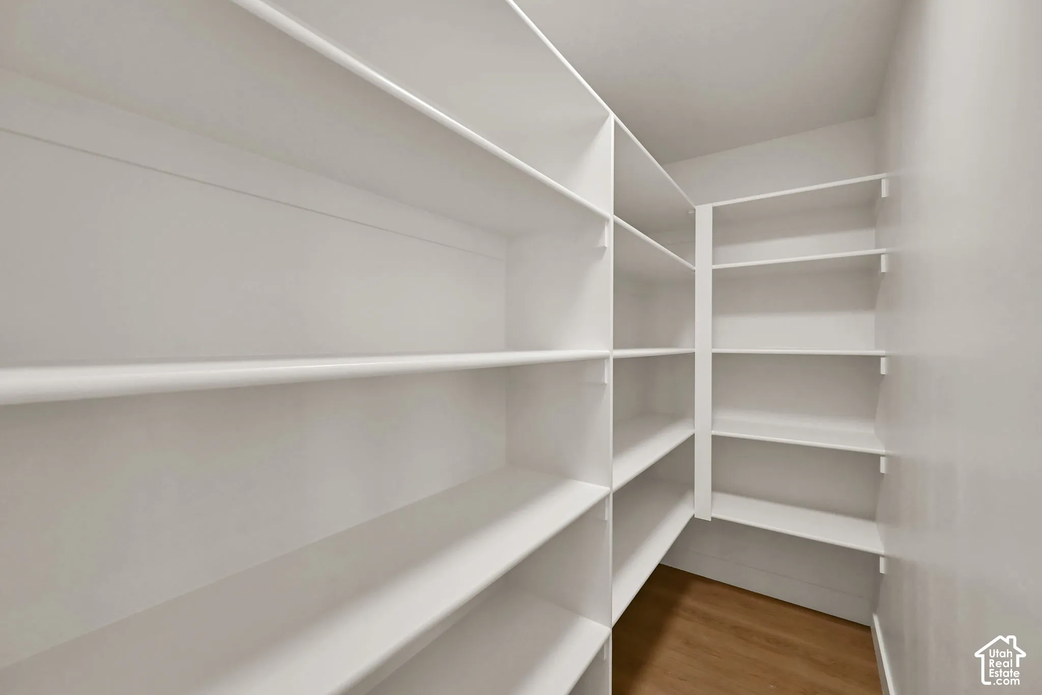 Walk-in storage area featuring white floor-to-ceiling built-in shelving and wood-finish flooring