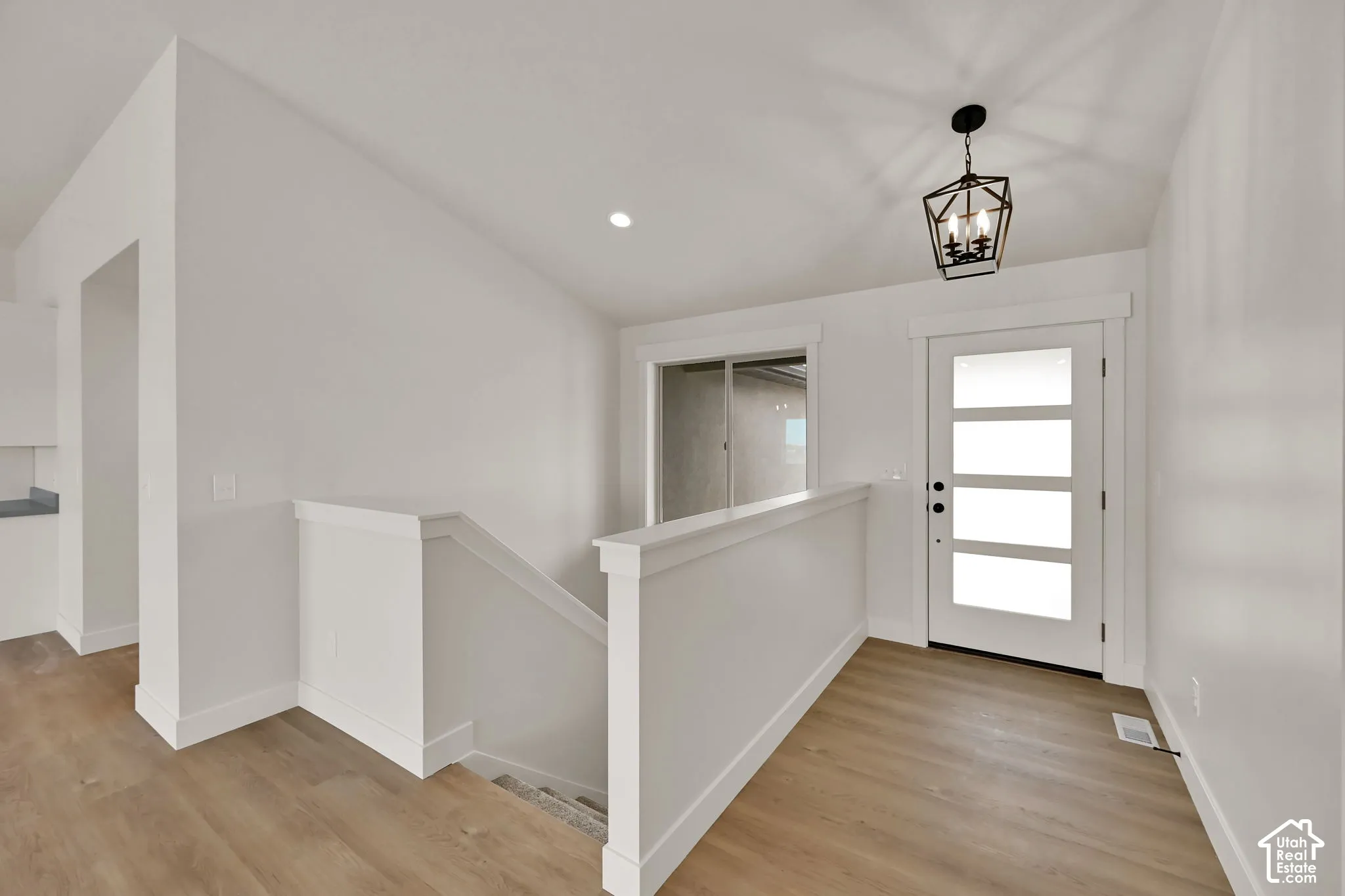 Entryway featuring wood-finish flooring, a geometric pendant light fixture, a paneled door with glass inserts, and a half-wall staircase enclosure