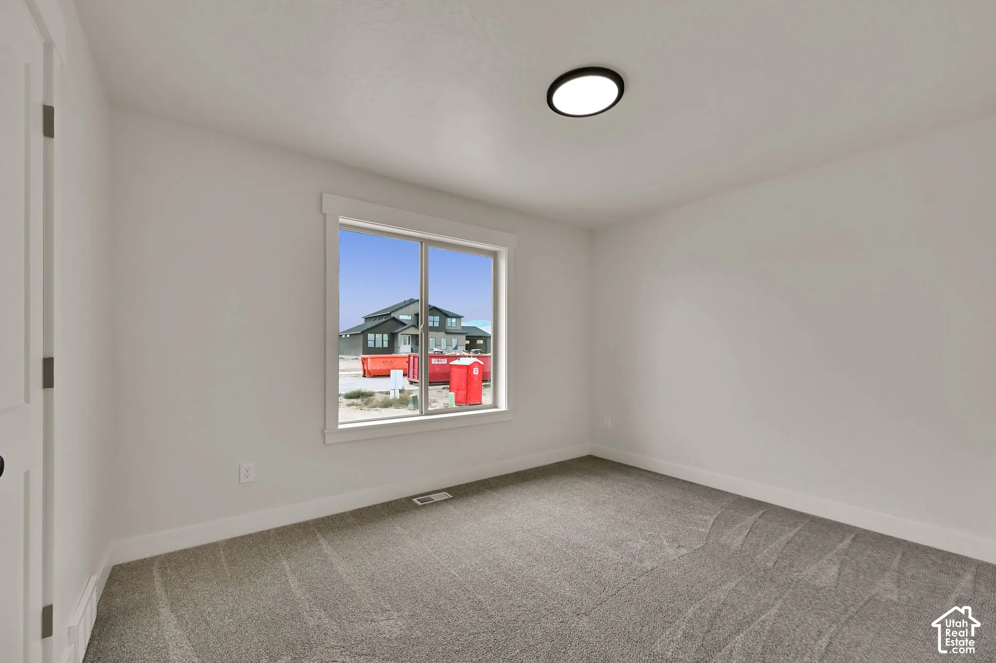 Neutral-toned interior room featuring wall-to-wall carpeting, a large sliding window with trim, and a flush-mount circular ceiling light