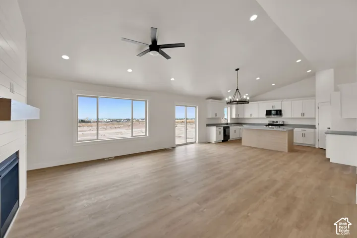 Open-concept interior featuring vaulted ceilings, wood-finish flooring, a kitchen island, recessed lighting, and a fireplace with shiplap detailing
