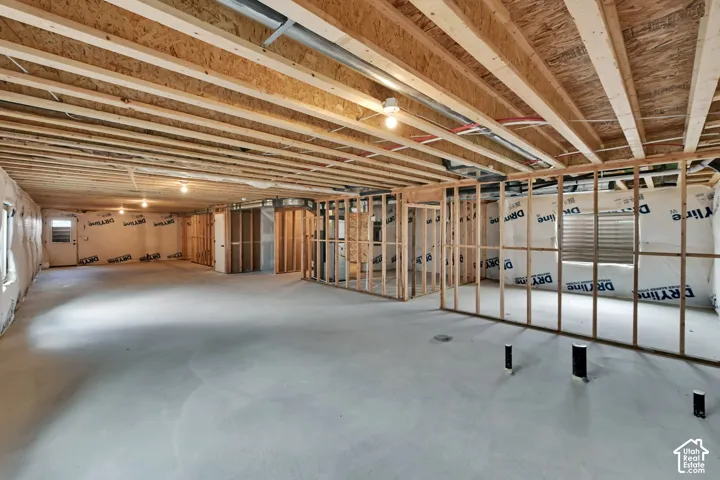 Unfinished interior space featuring exposed wood joist ceilings, concrete flooring, stud-framed partition walls, and installed drainage plumbing