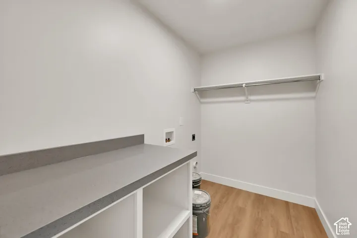 Laundry space featuring wood-finish flooring, white built-in cabinetry, solid surface countertop, and an integrated hanging rod