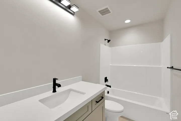 Bathroom featuring a vanity with a white countertop and rectangular undermount sink, matte black hardware, multi-bulb vanity light, and a white tub-shower surround