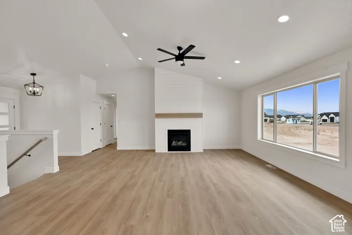 Vaulted ceilings with recessed lighting, shiplap fireplace surround, wood-finish flooring, ceiling fan, and large picture window