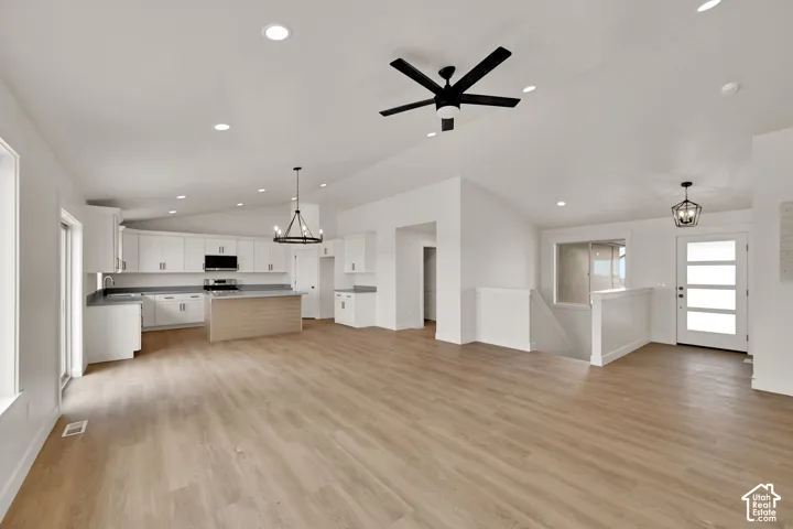 Open-concept interior featuring vaulted ceilings, wood-finish flooring, recessed lighting, and a kitchen equipped with white cabinetry, a center island, and a multi-light chandelier