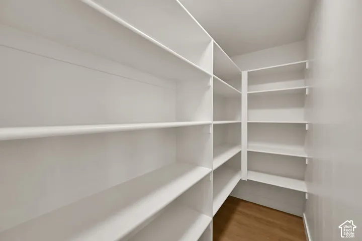 Walk-in storage area featuring white floor-to-ceiling built-in shelving and wood-finish flooring