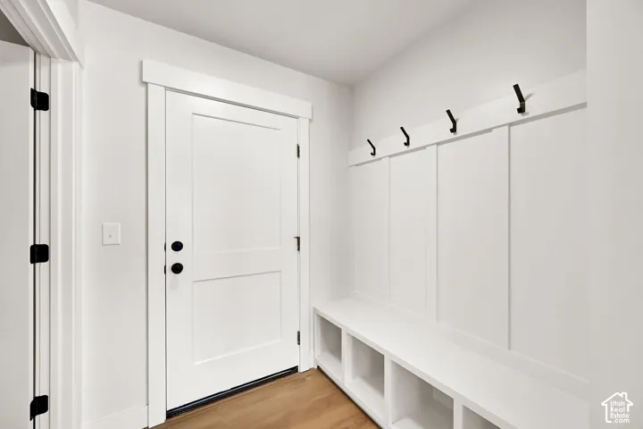 Entryway featuring a solid-core door with matte black hardware, built-in mudroom bench with integrated cubbies, board and batten wall paneling, and wood-finish flooring