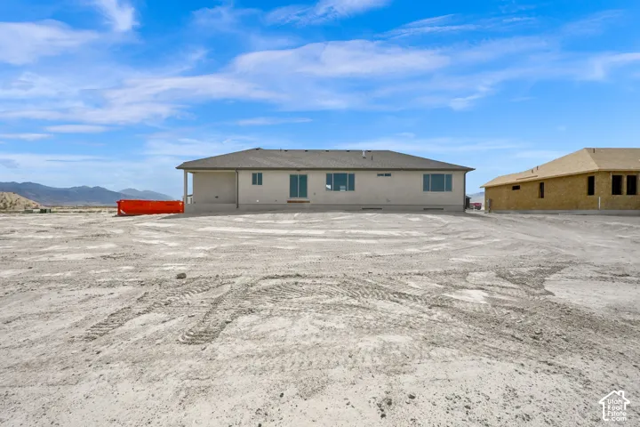 Single-story exterior featuring light-toned stucco siding, a hip roof with asphalt shingles, sliding glass doors, and expansive lot space with mountain backdrops