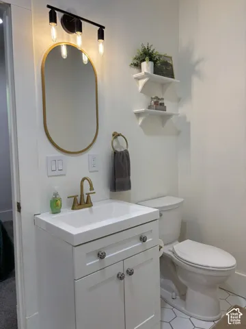 White vanity with an integrated sink and brass-finish faucet, hexagonal floor tiling, and a gold-framed oval mirror with a black-finish light fixture