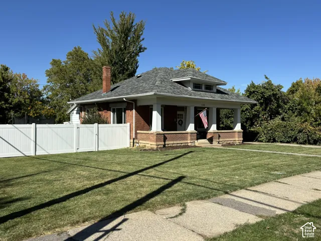 Brick exterior, columned front porch, low-pitch hipped roof, white privacy fence, and mature landscaping