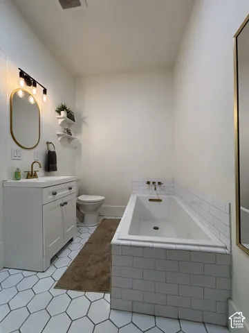 White hexagonal floor tiling, white subway-tiled bath surround, built-in bathtub, single vanity with shaker-style cabinetry, and wall-mounted light fixture